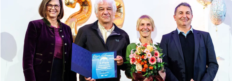 vier Personen mit Urkunde und Blumenstrauß