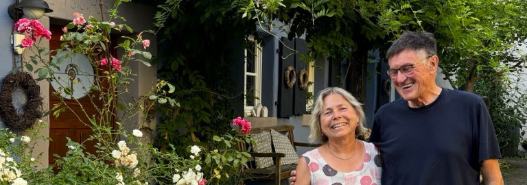 Mann und Frau vor Hauseingang mit Rosen und Goldregen davor