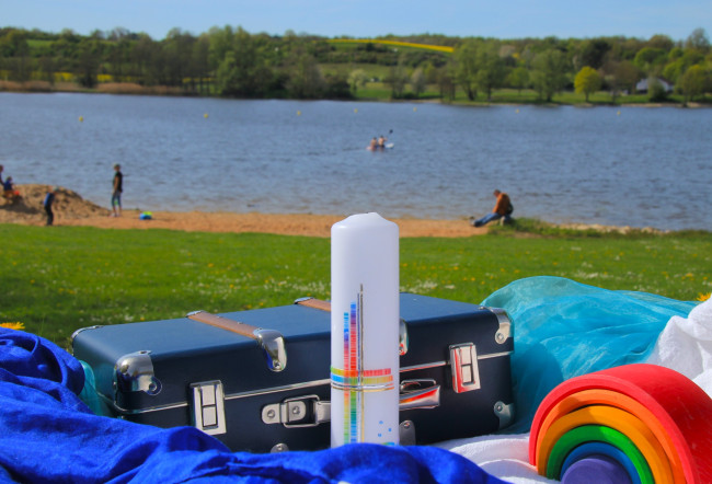 Taufkerze und Koffer vor See